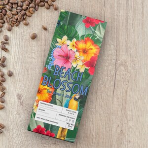May include: A package of "Beach Blossom" whole bean coffee with a tropical floral design, including hibiscus and a parrot. The package is green with the words "Beach Blossom" in blue. Coffee beans are scattered around the package on a wooden surface. Net Wt. 12 oz.