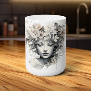 Peut inclure: Une tasse en céramique blanche avec une illustration en noir et blanc d'une femme avec des fleurs dans les cheveux. La femme a une expression douce et rêveuse.