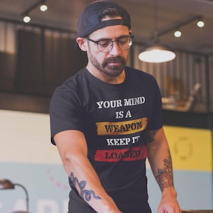 May include: Black t-shirt with the text "YOUR MIND IS A WEAPON KEEP IT LOADED" in white, yellow, and red. The shirt is a crew neck style.