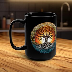 Può includere: Tazza in ceramica nera con un design colorato dell'albero della vita. L'albero è circondato da un motivo a nodo celtico e presenta un motivo di sole e luna.