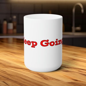 Könnte beinhalten: Weiße Keramik-Kaffeetasse mit dem Text "Keep Going" in roten Buchstaben.