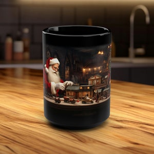 Könnte beinhalten: Schwarze Keramik-Tasse mit einer detaillierten Illustration von Santa Claus in seiner Werkstatt. Das Kunstwerk zeigt Santa im roten Anzug und weißem Bart, umgeben von Miniaturgebäuden und Spielzeug, mit weihnachtlichem Thema.
