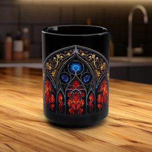 Könnte beinhalten: Schwarze Keramiktasse mit einem Buntglasdesign, das einen blauen, roten und gelben Bogen mit komplizierten Details zeigt.