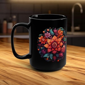 Könnte beinhalten: Schwarze Keramiktasse mit einem farbenfrohen Blumendesign, das eine große orangefarbene Blume zeigt, die von kleineren Blumen und Blättern umgeben ist.