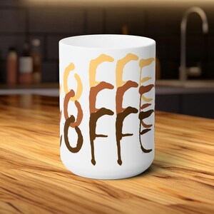 Könnte beinhalten: Weiße Keramik-Kaffeetasse mit dem Wort "COFFEE" in braunen, orangen und gelben Farbschleudern.