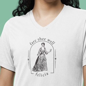 May include: White V-neck t-shirt featuring a black and white illustration of a woman with the text "fare thee well felicia". The graphic is enclosed in an arched frame. The shirt is made of a soft material.