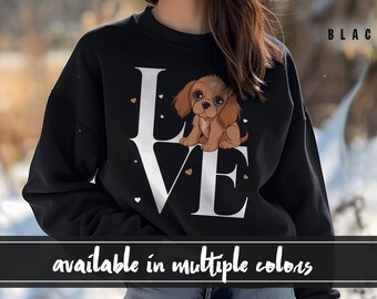 May include: Black sweatshirt with a white "LOVE" graphic featuring a brown and white puppy inside the "O". The sweatshirt has small white hearts scattered around the graphic. The text "BLACK" appears in the top right corner of the image. The text "available in multiple colors" appears at the bottom of the image.