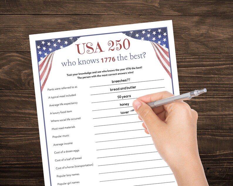 May include: A white paper game sheet with the text "USA 250 who knows 1776 the best?" is being filled out with a pen. The sheet has a blue border with stars and stripes, and includes trivia questions about the year 1776.