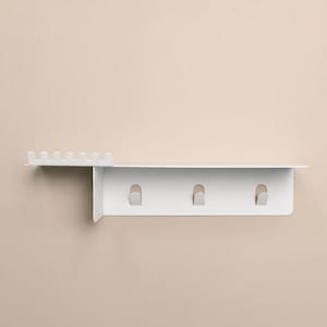 Pu&ograve; includere: Una mensola da parete in metallo bianco dotata di una superficie superiore piatta, una sezione laterale con sei piccole fessure verticali per organizzare oggetti e un pannello inferiore dotato di tre ganci integrati per appendere vari articoli.