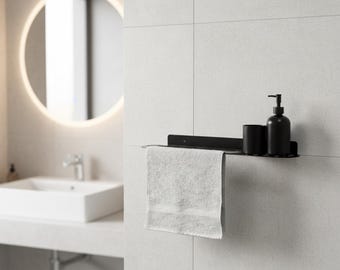 May include: A matte black metal wall-mounted shelf featuring a horizontal bar for hanging a light gray hand towel. The shelf surface holds a matching black cylindrical cup and a black soap dispenser with a pump mechanism for bathroom storage.