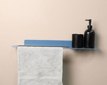 May include: A blue metal wall-mounted shelf featuring a horizontal bar for hanging a white towel. A black soap dispenser and a matching black cylindrical container are positioned on the flat surface of the shelf.