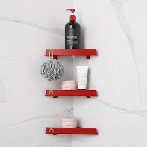 May include: Red corner shower shelves with a shampoo bottle, cream jars, and a body sponge. The shelves are mounted on a white tiled wall. The shampoo bottle is black with red accents.