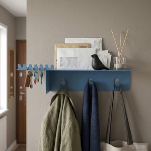 May include: A blue metal wall shelf with key hooks, a lower row of hooks, and a top shelf. The shelf holds keys, mail, a black bird figurine, and a glass diffuser. A green jacket, blue scarf, and a tote bag hang below.