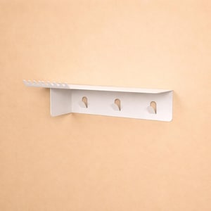 Puede incluir: Un estante de pared blanco con una superficie superior plana y un panel trasero vertical. El estante incluye una fila de peque&ntilde;as muescas en el lado izquierdo y tres ganchos integrados espaciados uniformemente en el panel vertical.