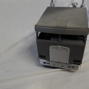 May include: A gray toy semi-truck with a detailed design. The truck features a cab with a roof, windows, and a front grill. The front bumper and other details are visible. The toy is likely made of plastic.