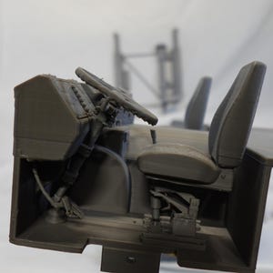 May include: A gray 3D-printed model of a vehicle interior, featuring a steering wheel, seats, and dashboard. The model is detailed, showing the structure of the components. The overall theme is automotive or engineering.