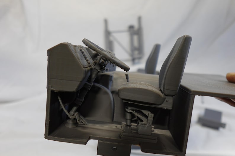 May include: A gray 3D-printed model of a vehicle interior, featuring a steering wheel, seats, and dashboard. The model is detailed, showing the structure of the components. The overall theme is automotive or engineering.