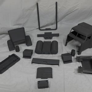 May include: A collection of grey plastic vehicle interior components, including a seat, dashboard parts, and a cab frame, laid out on a white surface. These appear to be model or prototype parts.