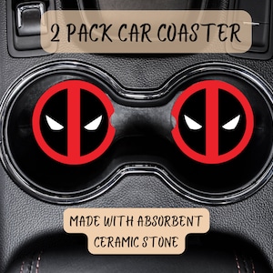 May include: Two red and black car coasters with a Deadpool logo. The coasters are made with absorbent ceramic stone. The text "2 PACK CAR COASTER" is at the top of the image. The text "MADE WITH ABSORBENT CERAMIC STONE" is at the bottom of the image.