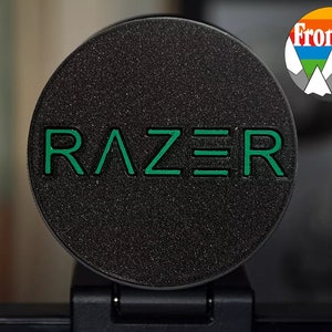 May include: A black round Razer webcam cover with the Razer logo in green.