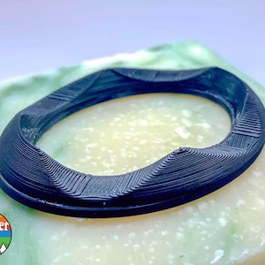 May include: A black 3D printed ring with a textured surface. The ring is sitting on a green and white surface.
