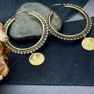 Peut inclure: Une paire de boucles d'oreilles créoles dorées avec un design détaillé et un pendentif en forme de globe.