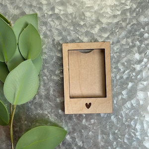 May include: A wooden picture frame with a heart cutout at the bottom. The frame is light brown and has a natural wood finish.
