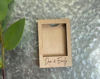 May include: A wooden picture frame with a cutout for a photo. The frame is light brown and has the text "Dan & Emily" engraved on the bottom.