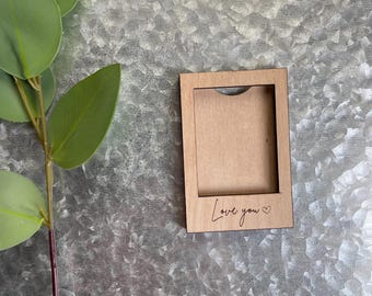 May include: A small wooden frame with a cutout for a photo. The frame is brown and has the words "Love you" engraved on the bottom with a small heart symbol.