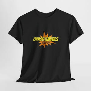 Puede incluir: Una camiseta negra de manga corta con un gráfico en el pecho. El diseño consiste en una forma de estrella naranja con el texto amarillo "OPPORTUNITIES" en una fuente estilo cómic, y la palabra "GOD OF" en un texto amarillo más pequeño.