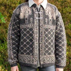 Peut inclure: Un gilet en tricot gris anthracite et beige avec un motif à losanges répétitif, des motifs de béliers stylisés sur la poitrine et une chemise à col blanc en dessous. Le gilet a des manches longues, un ourlet côtelé et deux fermoirs en métal argenté.
