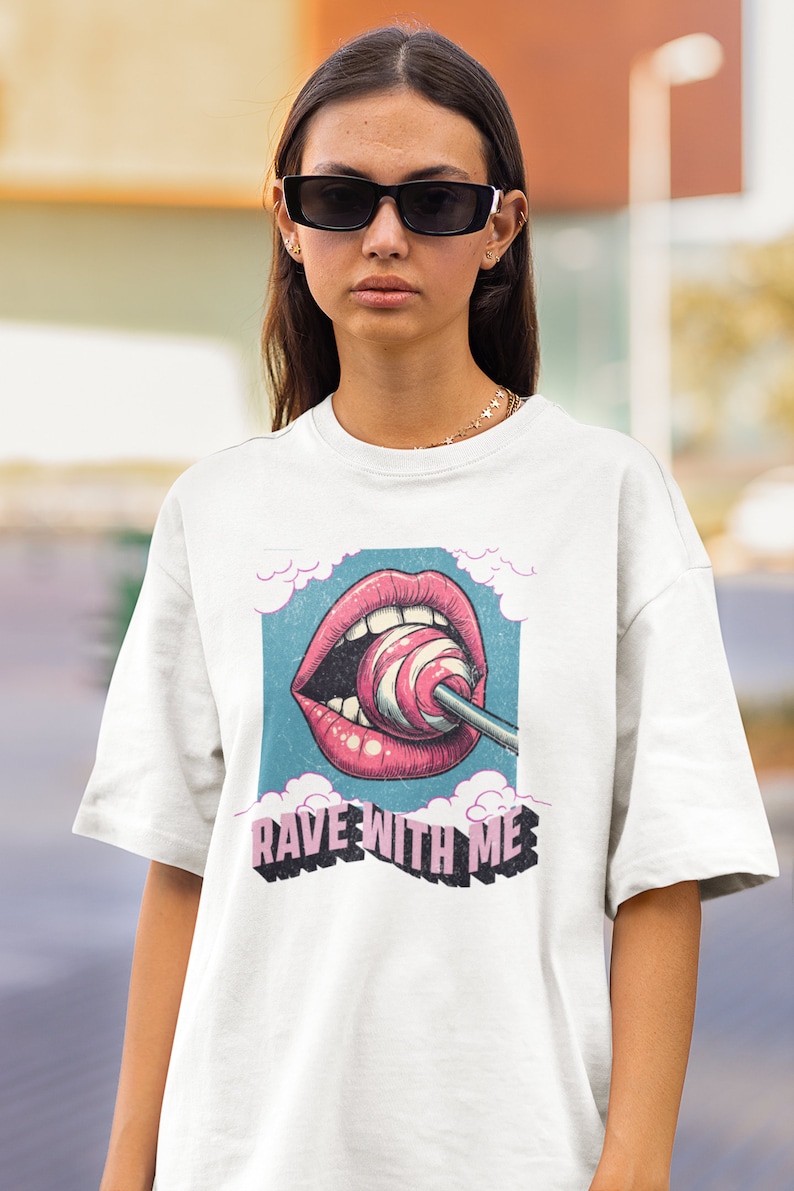 May include: White t-shirt featuring a graphic of a pink mouth with a lollipop and the text "Rave With Me" in pink and black lettering.