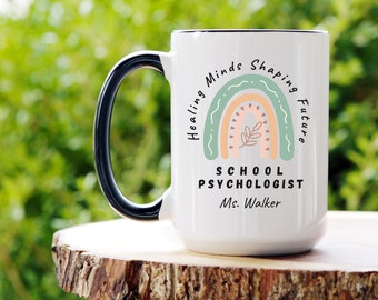 May include: White ceramic coffee mug with a black handle. The mug has a rainbow design with the text "Healing Minds Shaping Future" and "School Psychologist Ms. Walker".