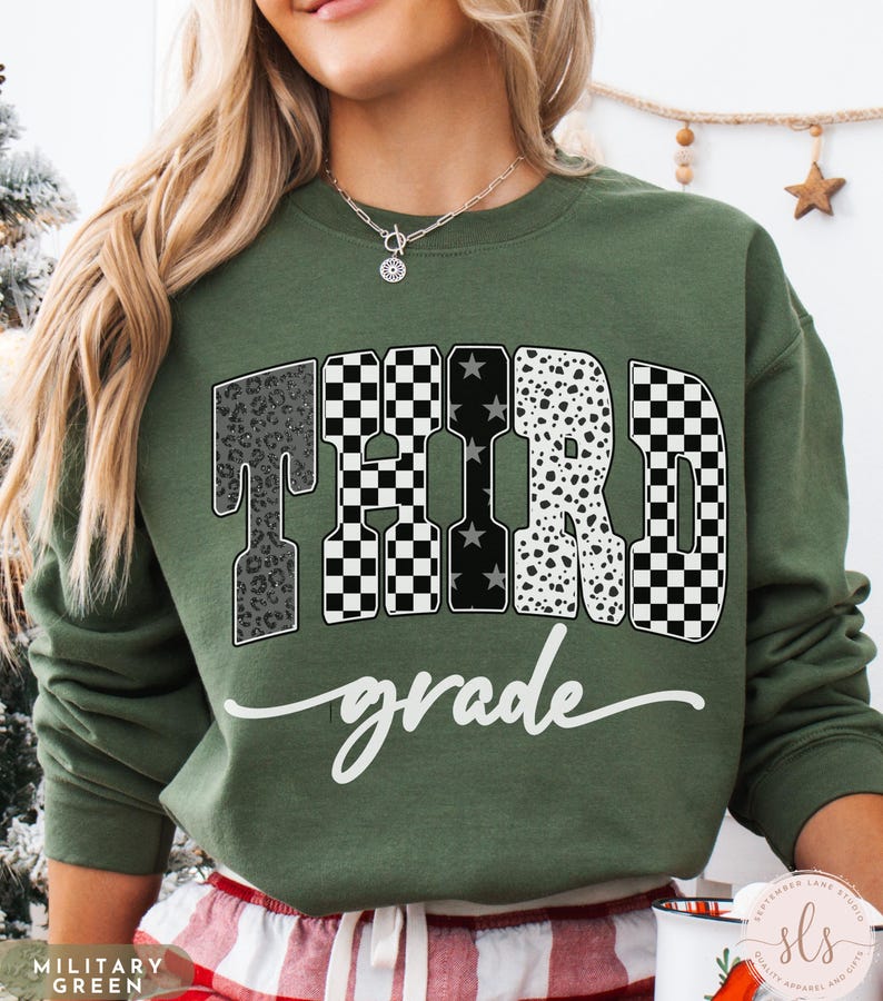 May include: An olive green sweatshirt with the words "THIRD grade" in a mix of patterns, including leopard print, checkered, and polka dots. The word "grade" is in a cursive font. The sweatshirt is a casual style.