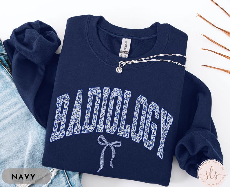 May include: Navy blue sweatshirt with a white floral pattern spelling out "RADIOLOGY" with a white bow on the front.