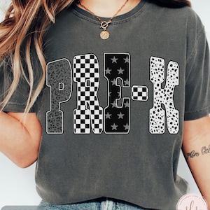 May include: A dark gray t-shirt with the word "PRE-K" in a bold, patterned design. The letters feature leopard print, checkered, star, and dalmatian patterns. The word "PEPPER" is printed at the bottom of the shirt.