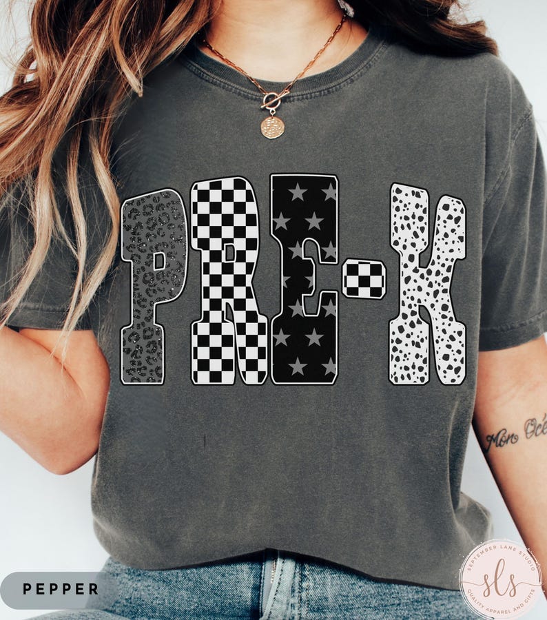 May include: A dark gray t-shirt with the word "PRE-K" in a bold, patterned design. The letters feature leopard print, checkered, star, and dalmatian patterns. The word "PEPPER" is printed at the bottom of the shirt.