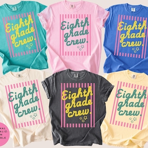 May include: A collection of six short-sleeved crew neck t-shirts in teal, pink, blue, cream, charcoal, and yellow. Each shirt features a central graphic with vertical pink stripes, the text "Eighth grade crew." in script, and small star icons.