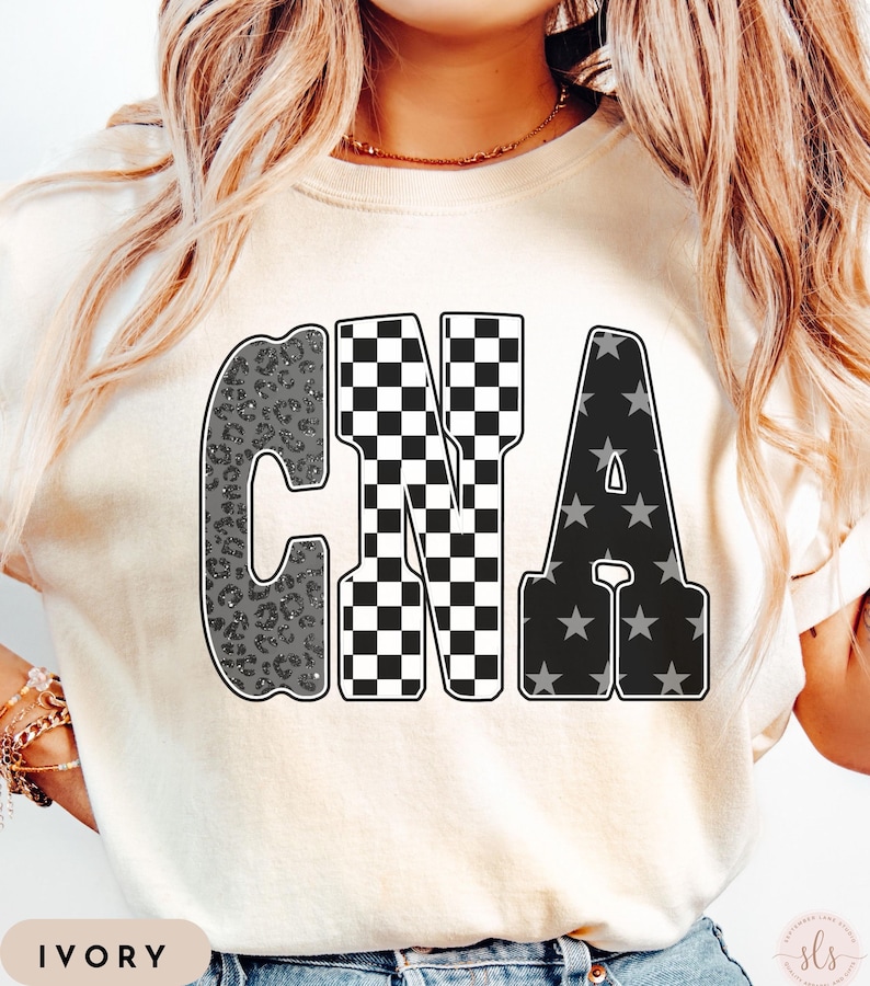 May include: Ivory-colored t-shirt with the letters "CNA" in a bold, outlined font. The "C" has a gray leopard print, the "N" is a black and white checkerboard pattern, and the "A" features gray stars on a black background. The word "IVORY" is at the bottom.