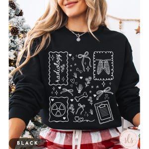 Puede incluir: Sudadera negra con dise&ntilde;os gr&aacute;ficos blancos relacionados con la radiolog&iacute;a. El dise&ntilde;o incluye la palabra "radiology", huesos, corazones, lazos, flores y una imagen de rayos X. La esquina inferior izquierda de la sudadera dice "BLACK".