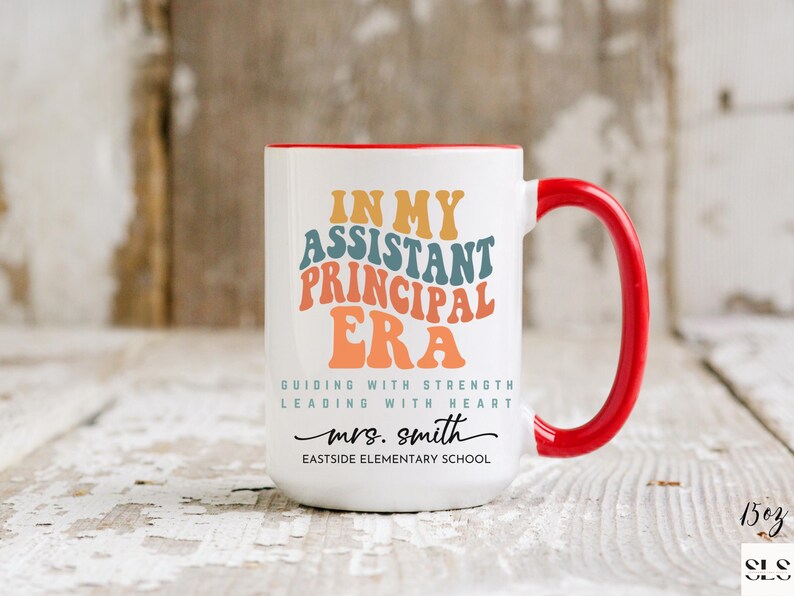 May include: White ceramic coffee mug with a red rim and handle. The mug has a colorful graphic that says "In My Assistant Principal Era" with the text "Guiding with Strength Leading with Heart" and "mrs. smith Eastside Elementary School".