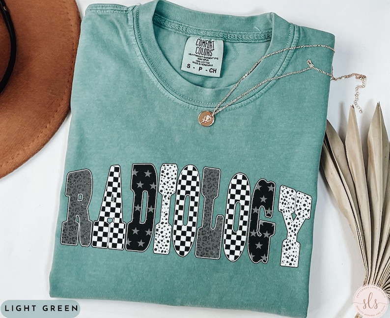 K&ouml;nnte beinhalten: Hellgr&uuml;nes T-Shirt mit dem Wort "RADIOLOGY" in einem auff&auml;lligen, gemusterten Design. Die Buchstaben zeigen eine Mischung aus karierten, Leopardenmuster- und Sternmustern. Eine goldene Halskette mit Anh&auml;nger liegt auf dem Shirt.