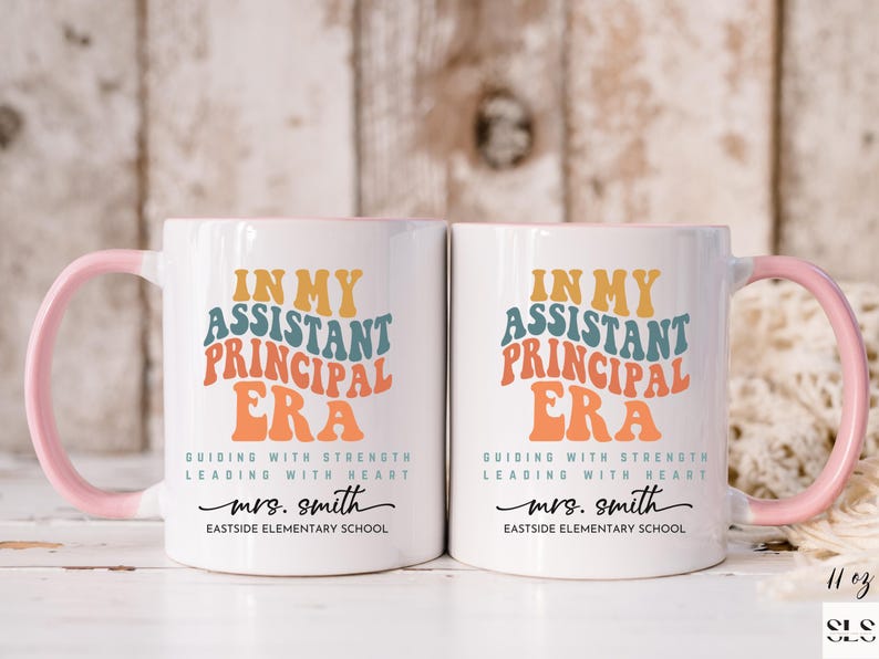 May include: Two white ceramic mugs with pink handles. The mugs feature a colorful graphic that says "In My Assistant Principal Era" with the text "Guiding with Strength Leading with Heart" and "mrs. smith Eastside Elementary School".