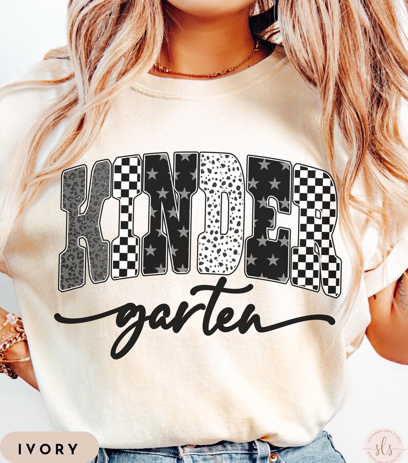 May include: Ivory-colored t-shirt with the word "KINDER" in a bold, multi-patterned design, including leopard print, checkered, and star patterns. The word "garten" is written in a cursive font below the word "KINDER".