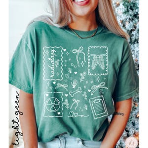 Puede incluir: Camiseta verde claro con ilustraciones gr&aacute;ficas blancas de elementos de tem&aacute;tica m&eacute;dica, incluyendo una caja tor&aacute;cica, huesos y una carpeta. La palabra "radiolog&iacute;a" est&aacute; escrita en la camiseta. Las palabras "verde claro" est&aacute;n escritas verticalmente en el lado izquierdo.