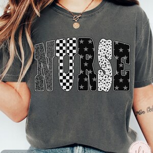 May include: Dark gray t-shirt with the word "NURSE" in large, bold letters. The letters have various patterns: leopard print, checkered, stars, and dalmatian spots. The shirt is a comfortable fit and has a round neckline.