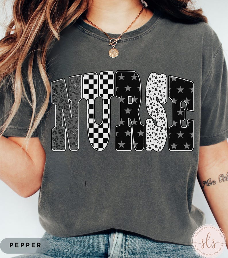 May include: Dark gray t-shirt with the word "NURSE" in large, bold letters. The letters have various patterns: leopard print, checkered, stars, and dalmatian spots. The shirt is a comfortable fit and has a round neckline.
