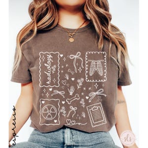 Puede incluir: Camiseta marr&oacute;n con un dise&ntilde;o gr&aacute;fico blanco que presenta la palabra "radiolog&iacute;a" e ilustraciones m&eacute;dicas. El dise&ntilde;o incluye huesos, una caja tor&aacute;cica y un s&iacute;mbolo de radiaci&oacute;n. La camiseta tiene un aspecto vintage y desgastado.