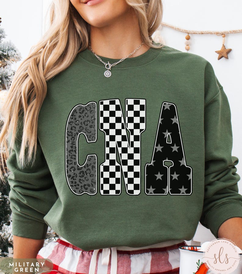 May include: Olive green sweatshirt with the letters "CNA" in a bold, decorative font. The "C" has a leopard print design, the "N" is checkered, and the "A" features a star pattern. The text "MILITARY GREEN" is at the bottom left.