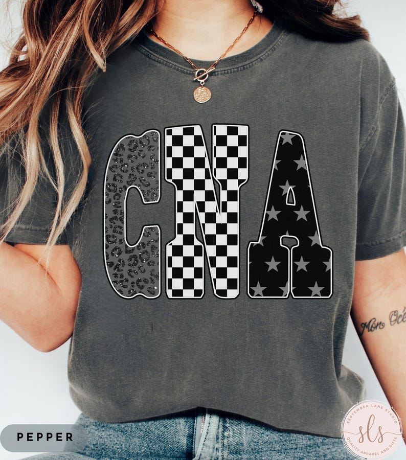 May include: Dark grey t-shirt with the letters "CNA" in a bold, outlined font. The "C" has a leopard print design, the "N" is checkered, and the "A" has a star pattern. The word "PEPPER" is at the bottom.